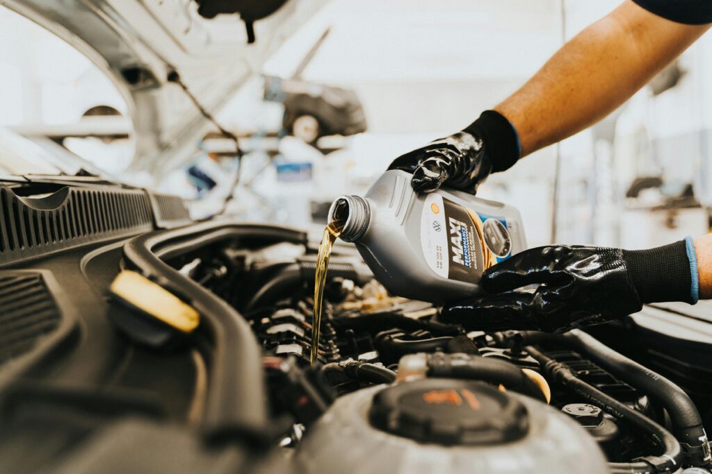 Why Regular Oil Changes Are Essential for Your Car – Finchley Park Autos Explains Close-up of a mechanic pouring engine oil into a car engine in an auto repair shop.